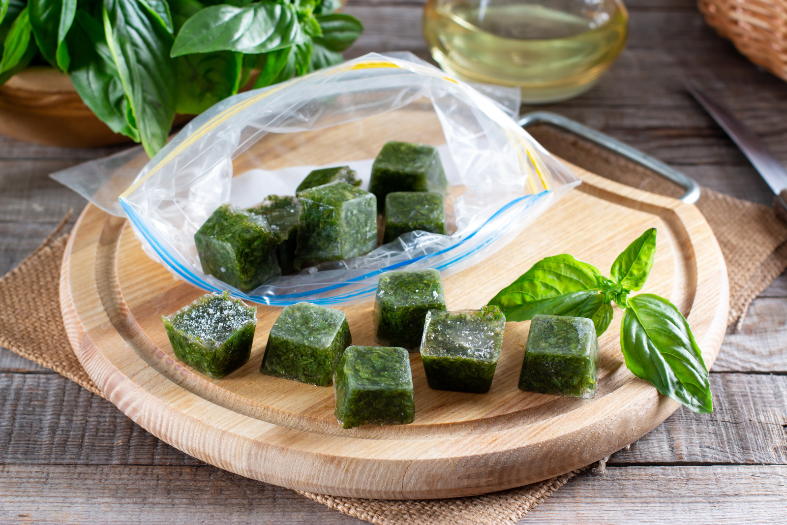 Frozen ice cubes of fresh herbs on a wooden cutting board with a burlap background and wood table underneath.