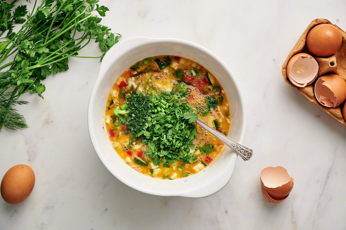 Egg and vegetable mixture in a white bowl with fresh chopped herbs on top.