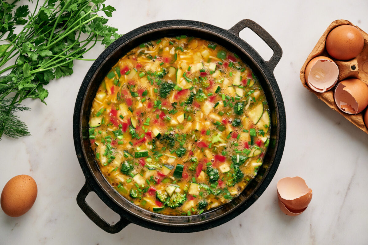 Scrambled egg and vegetable mixture in a cast iron skillet with open eggshells on the sides.