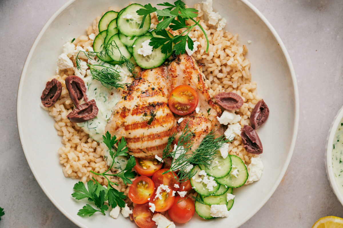 A white bowl filled with Greek Chicken, rice, and veggies. 