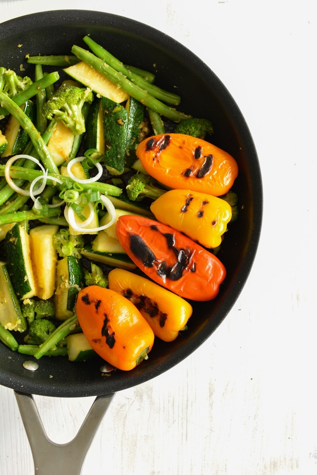 half view image of a bowl containing stir fried zucchini, broccoli, snap peas, with roasted bell peppers, 