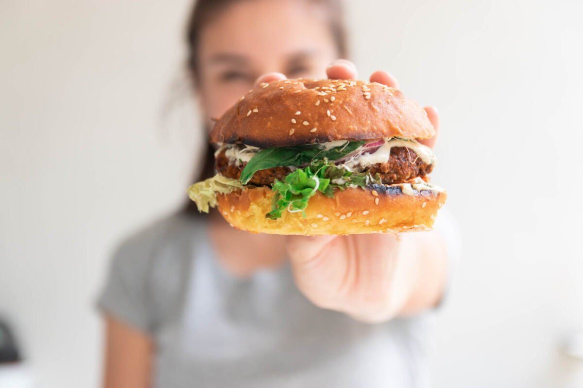 Woman holding a plat-based burger in her hand, out in front of her face.