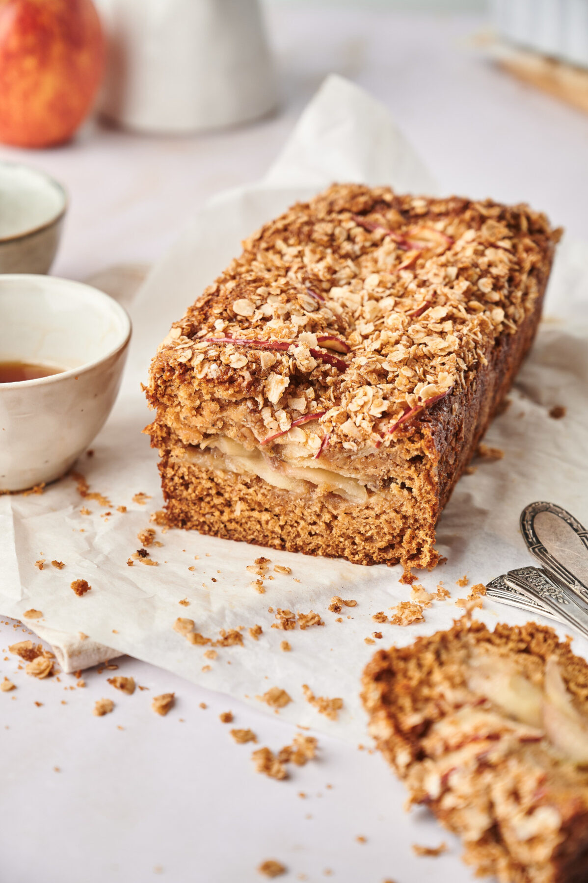 A loaf of healthy apple bread sliced with small bowls and parchment paper.