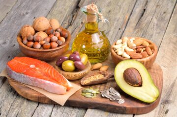 A wooden board with raw salmon, olives, avocado, olive oil, and assorted nuts.