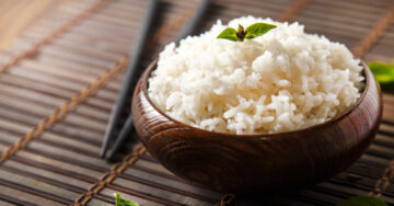 A bowl of fluffy jasmine rice on a bamboo mat with chopsticks in the background.