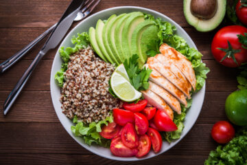 Healthy salad plate with quinoa, tomatoes, chicken, avocado, lime and mixed greens (lettuce, parsley) on wooden background.