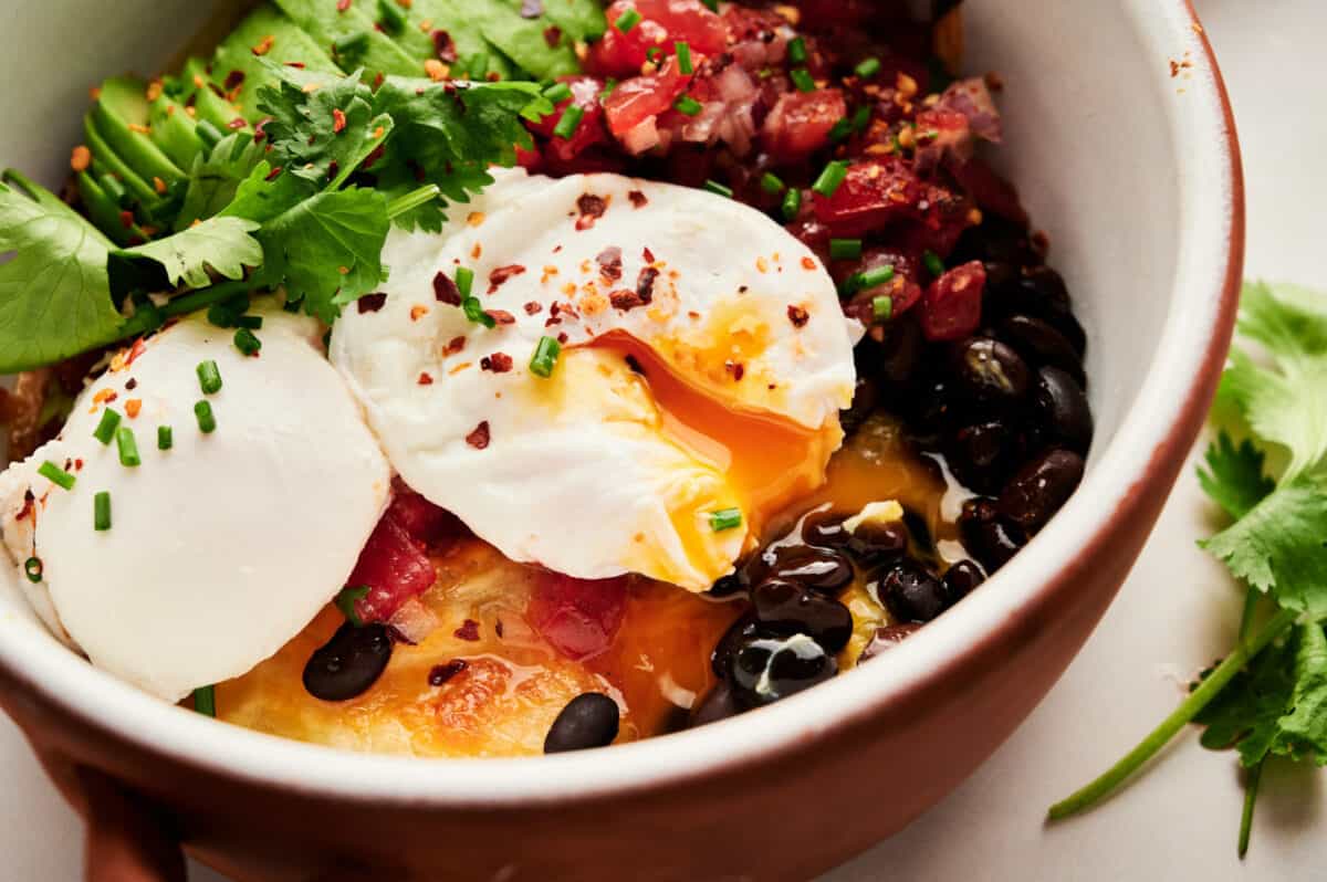 Healthy Spanish Huevos Rancheros with poached eggs, avocadoes, black beans, salsa, and cheesy potatoes.