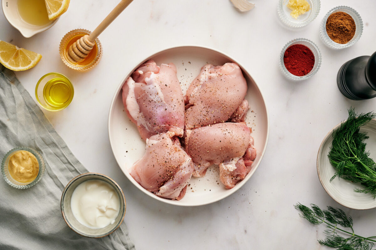 Chicken thighs on a white plate with seasonings.