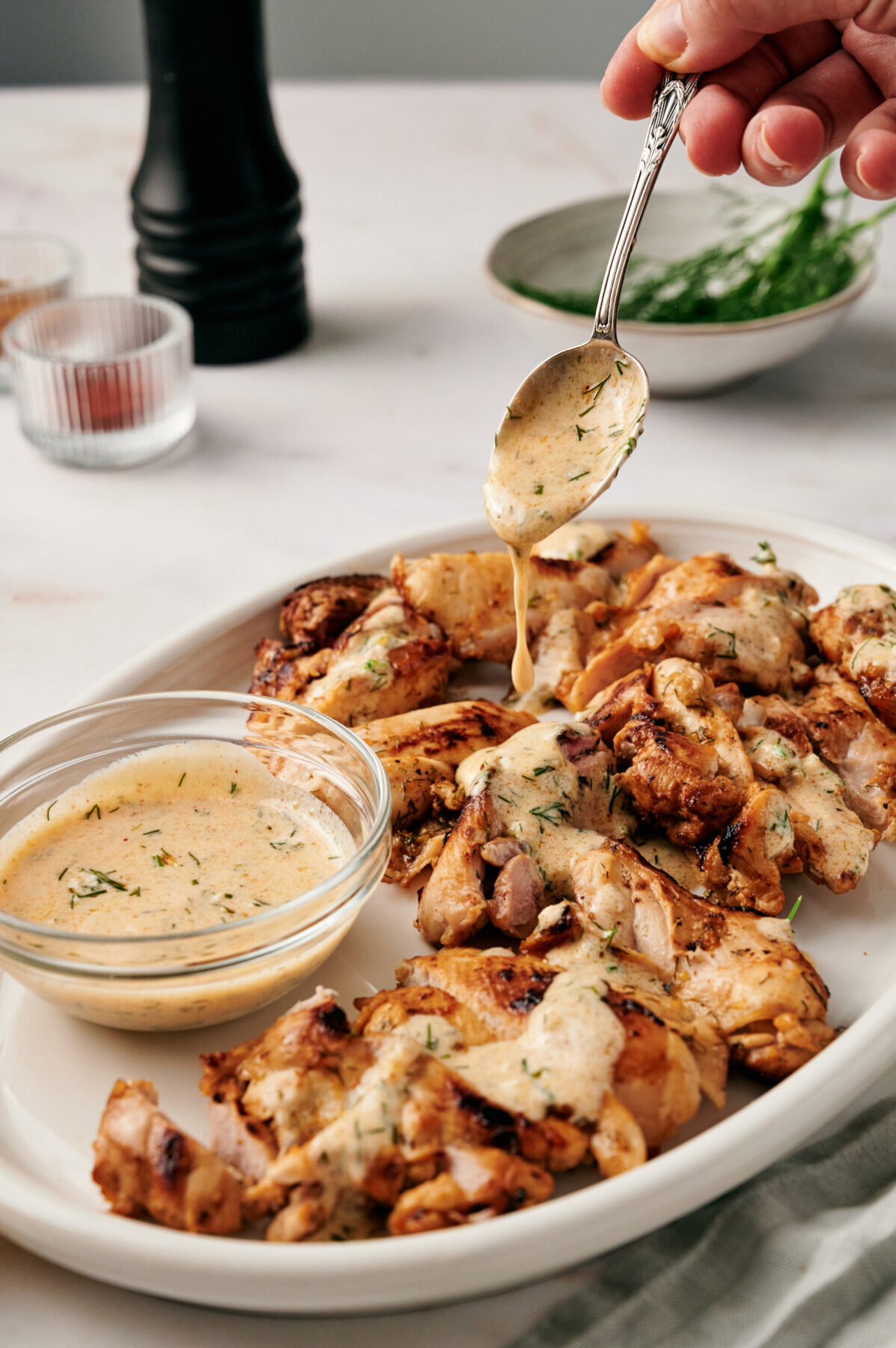 Lemon Dill Chicken on a white plate and a spoon drizzling Dijon yogurt sauce.