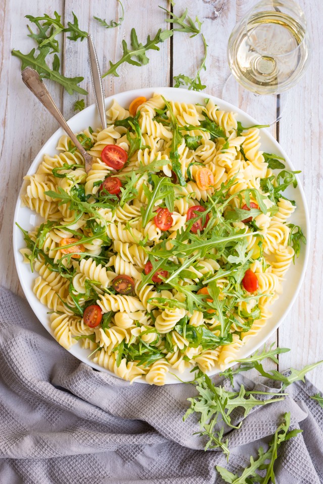 Top view of Lemon Arugula Pasta Salad on a white plate on a white wooden table with a glass of white wine.