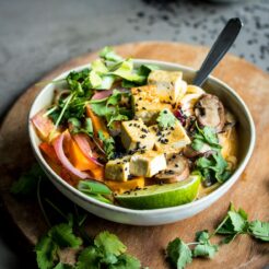 Lemongrass Coconut Noodle Soup in a bowl with a spoon on a wooden cutting board.