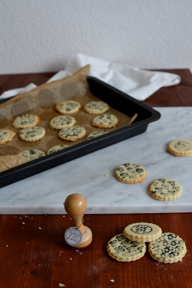 close-up view of freshly baked stamped marzipan layer cookies, some arranged on a baking tray, and others placed outside the tray
