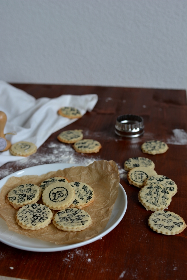 a batch of stamped marzipan layer cookies arranged on a plate, with some cookies scattered outside the plate
