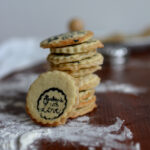 cropped image of a pile of stamped marzipan layer cookies with one cookie showing an intricate stamp design, and a dusting of flour near the pile