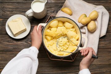 Woman preparing tasty mashed potatoes on wooden background.