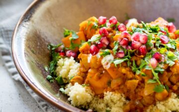 Sweet Potato and Chickpea Moroccan Style Stew in a tan glazed dish on top of a cloth napkin on a white speckled tabletop.