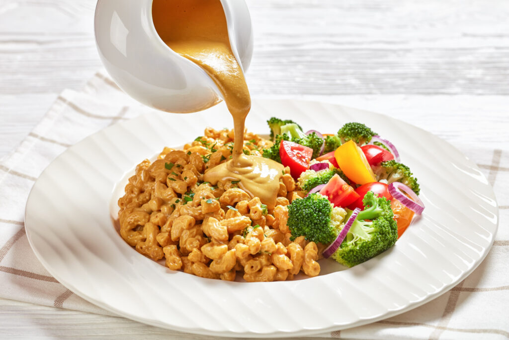 nutritional yeast sauce pouring over vegan mac and cheese