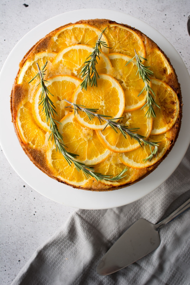 top down image of a mouthwatering orange upside-down cake adorned with rosemary sprigs.