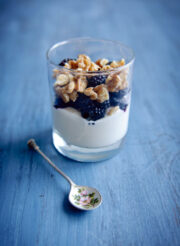 A parfait with granola and a metal spoon beside it.