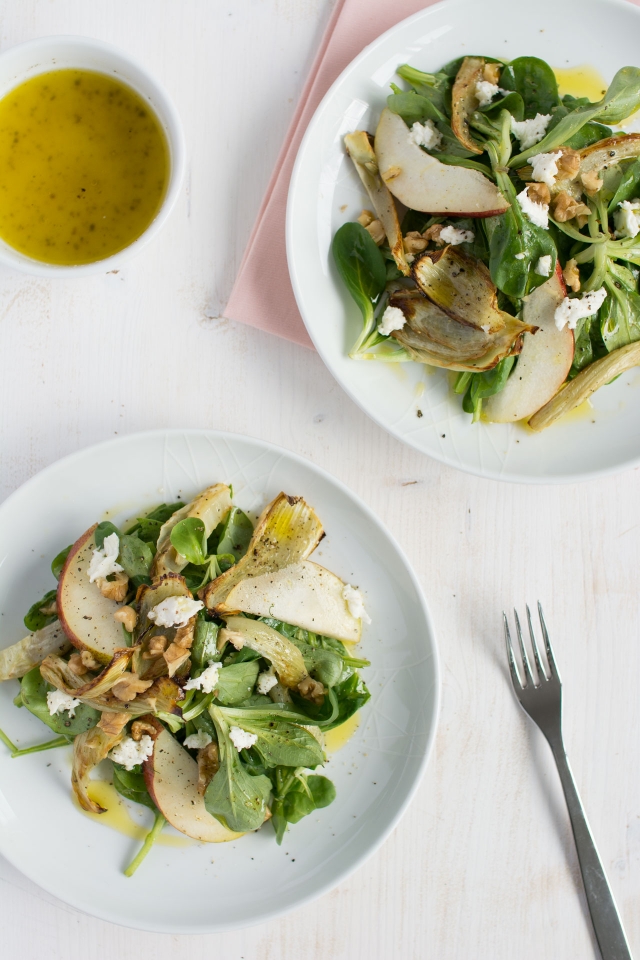 overhead image capturing two plates showcasing a delectable roasted fennel and pear salad, accompanied by a bowl of dressing
