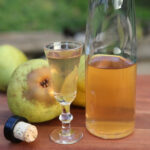 Spiced pear liqueur on a wooden cutting board with Bartlett pears in the background.