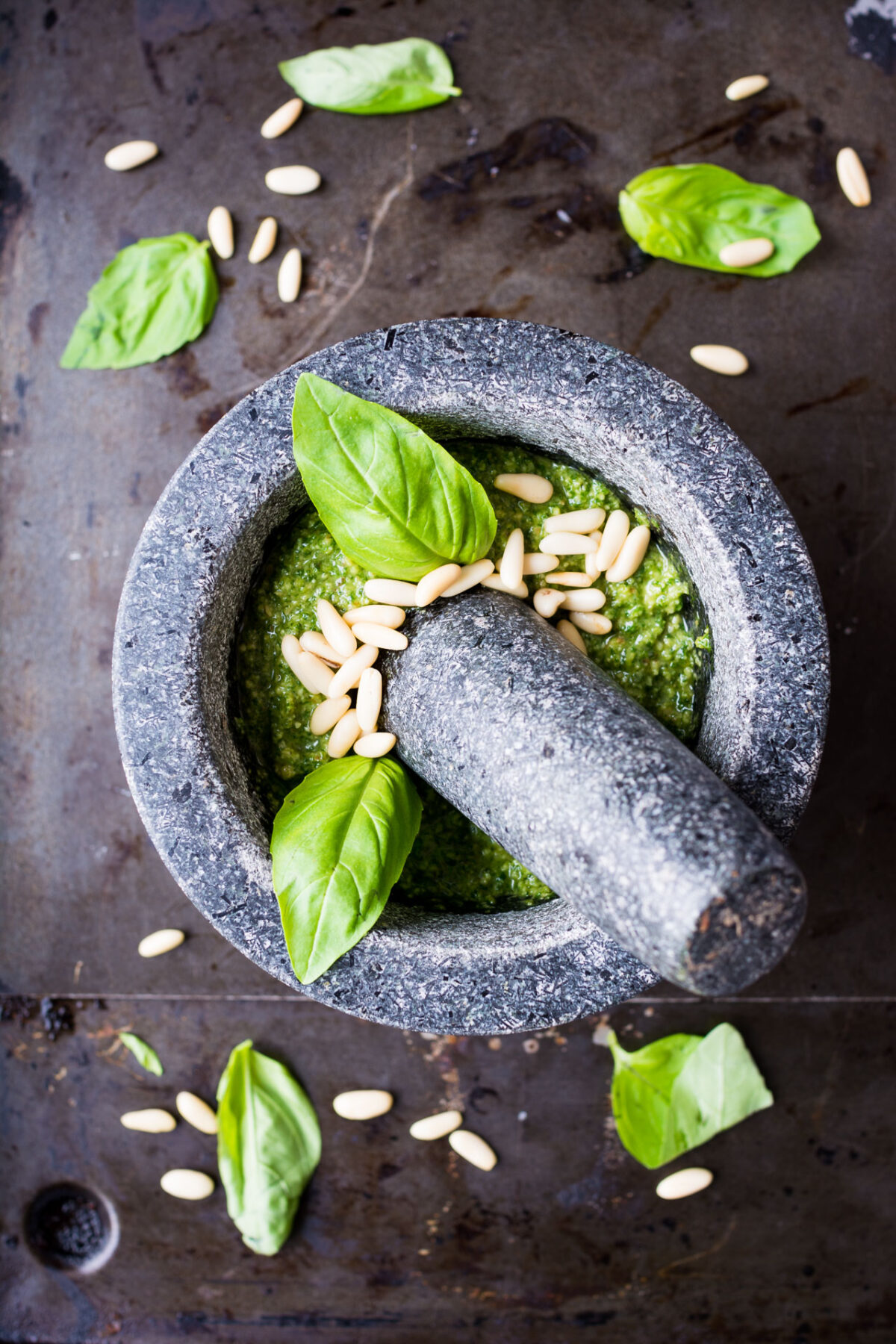 top down image of a stone mortar containing smooth mixture of pesto with basil leaves and pinenuts