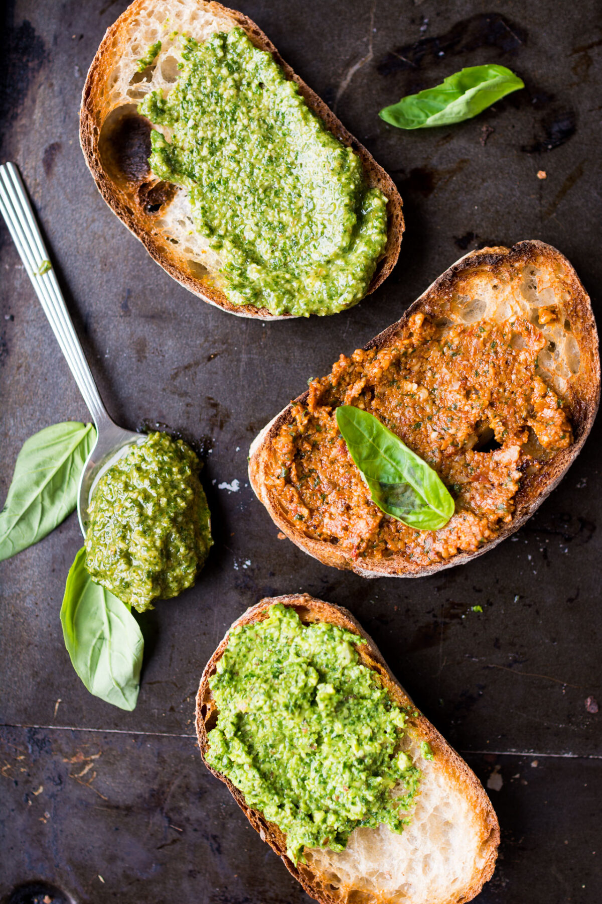 Three slices of bread with spread pesto - one with classic basil, one with zesty sun-dried tomato, and one with nutty spinach-wallnut ricotta variation