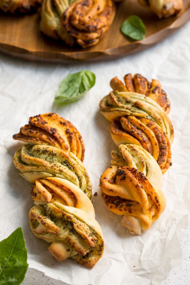 Close-up view of two-tone pesto bread twists on a white tablecloth.