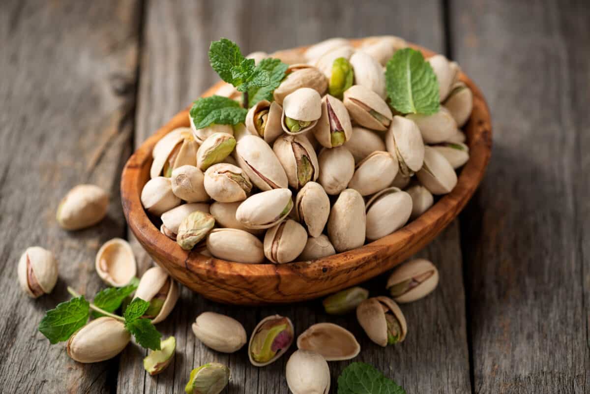 A wooden bowl filled with pistachios on a wooden table.