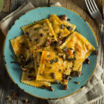 Horizontal view of pumpkin ravioli on a turquoise plate with a small pumpkin and sage on a wooden table.