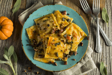 Horizontal view of pumpkin ravioli on a turquoise plate with a small pumpkin and sage on a wooden table.