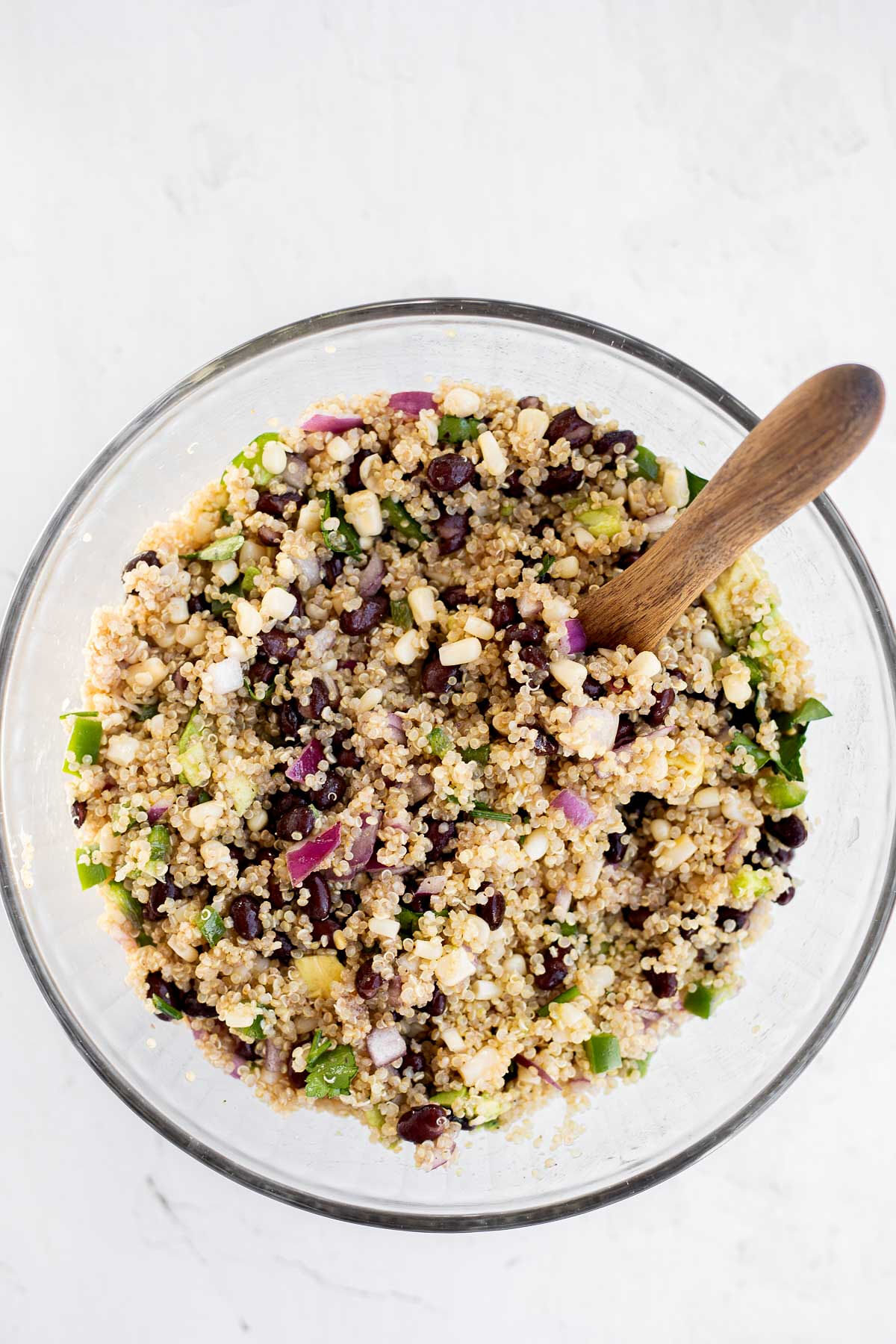 Mixing ingredients in a glass bowl for quinoa salad.