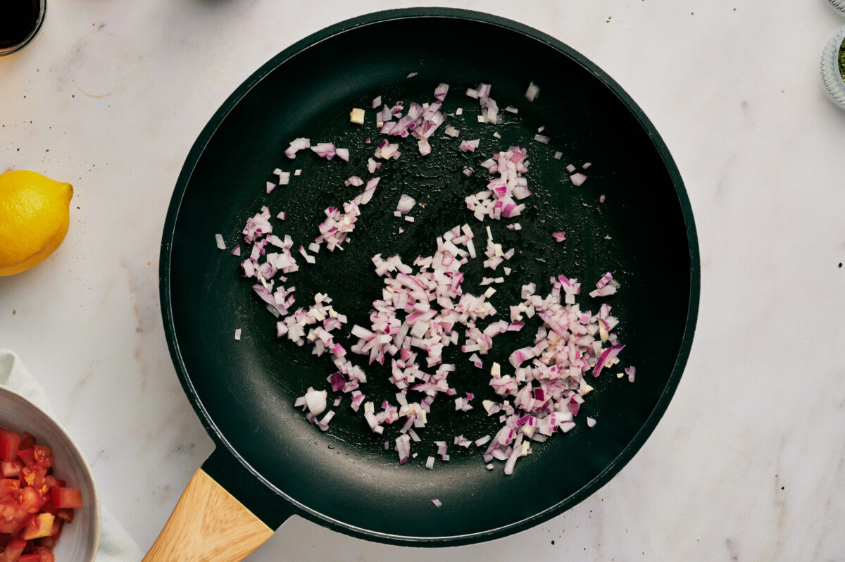 Onion being sautéed in a black skillet.