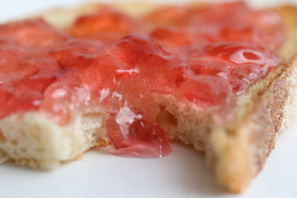 Closeup view of redbud jelly on toast with a bit taken out.