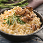 Creamy risotto in a black skillet garnished with rosemary and sautéed mushrooms.