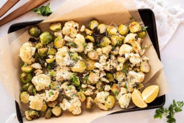 Roasted Cauliflower & Brussels Sprouts with Parmesan cheese on a parchment lined baking sheet.