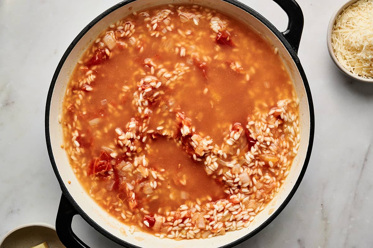 Additional stock added to the roasted tomato risotto in a large pan.