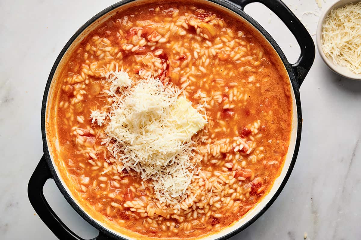 Parmesan cheese and butter added to the roasted tomato risotto in a large pan.