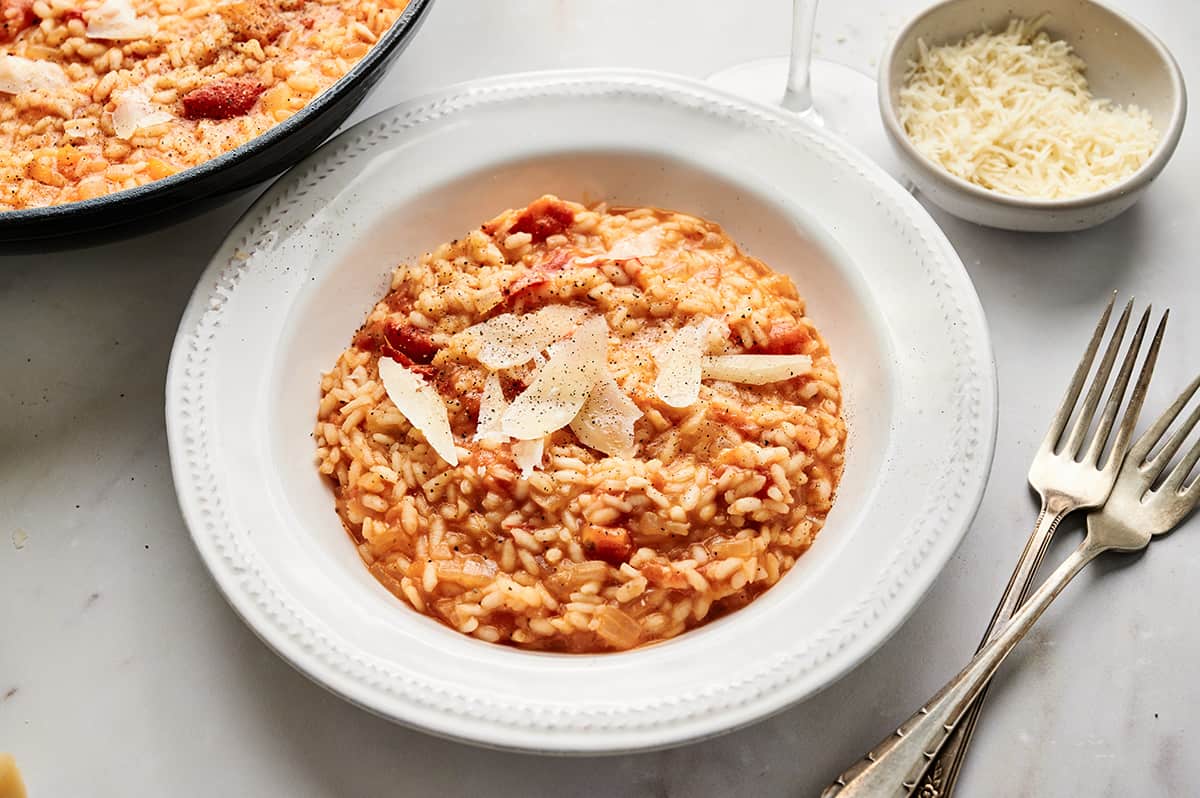 Roasted tomato risotto in a bowl, garnished with fresh Parmesan cheese flakes, salt, and pepper.