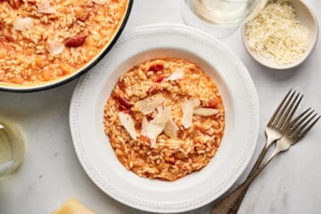 Roasted tomato risotto in a bowl, garnished with fresh Parmesan cheese flakes, salt, and pepper.