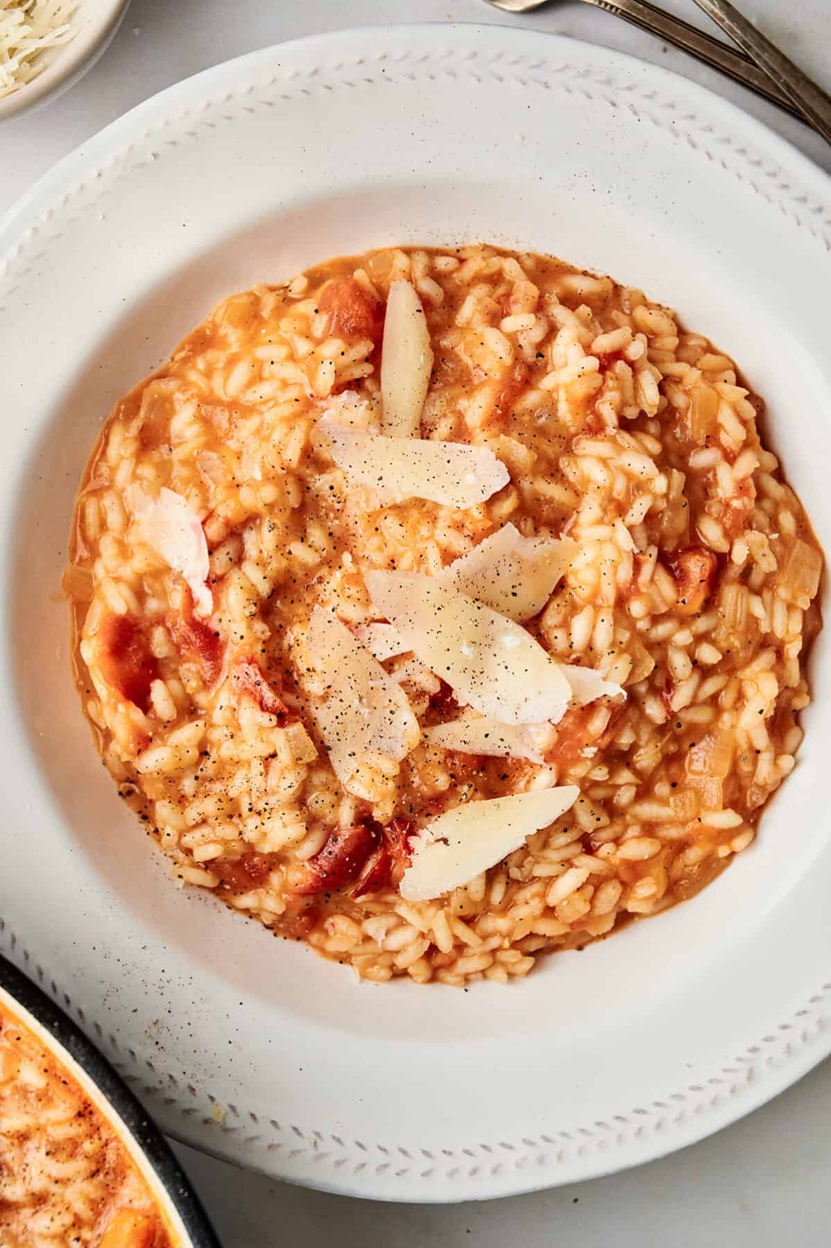 Roasted tomato risotto in a bowl, garnished with fresh Parmesan cheese flakes, salt, and pepper.