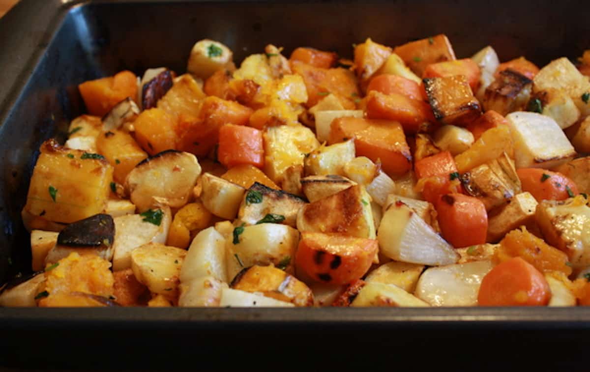 Roasted root vegetables seasoned with cardamom in a black roasting pan.