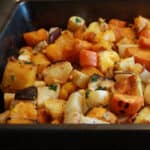 Roasted root vegetables seasoned with cardamom in a black roasting pan.