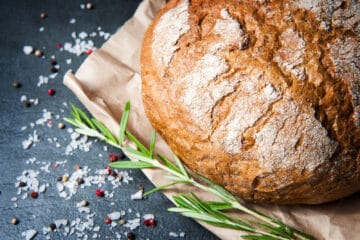 Loaf of Rosemary Bread with salt and pepper and a sprig of rosemary on paper.