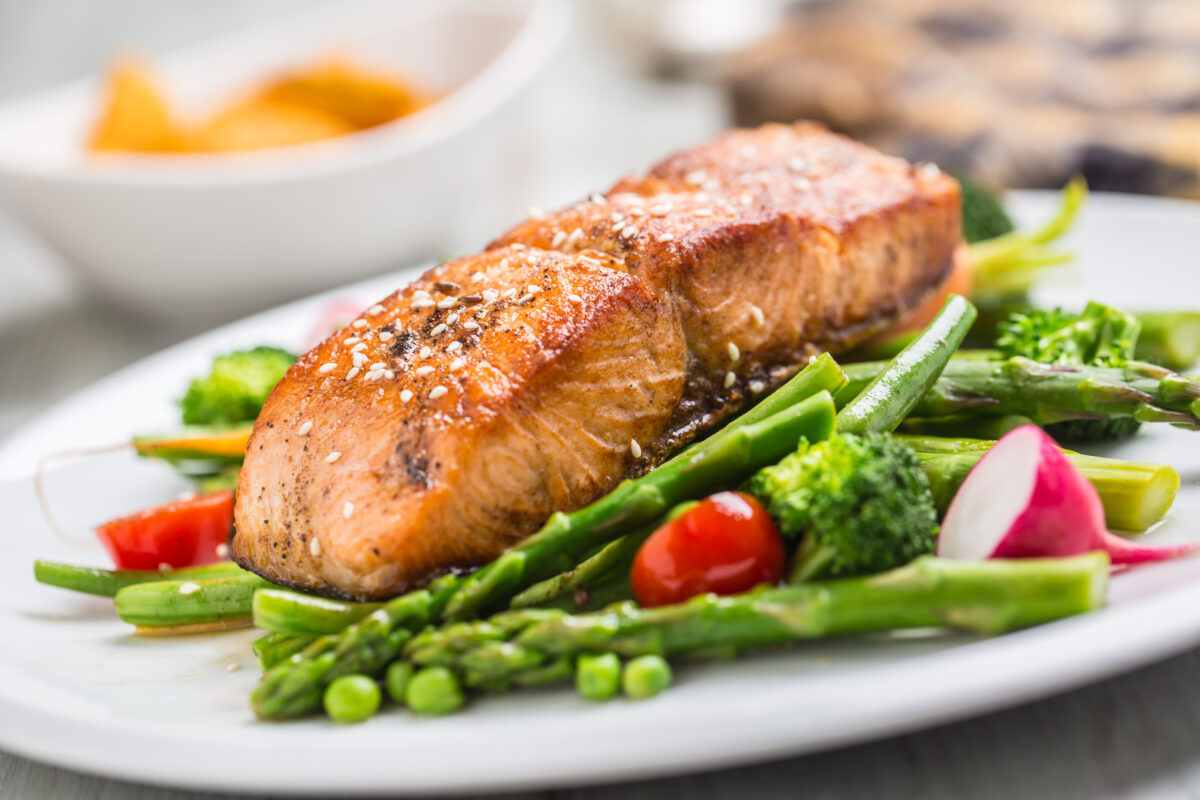 A strip of broiled salmon on a bed a vegetables on a white plate.