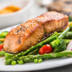 A strip of broiled salmon on a bed a vegetables on a white plate.