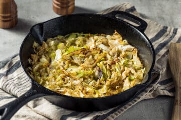 Sautéed green cabbage seasoned with salt and pepper in a cast iron pan.