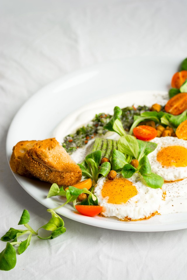 close up image of savory yogurt chimichurri salad, topped with spicy roasted chickpeas, slice avocado, tomatoes and eggs on the side
