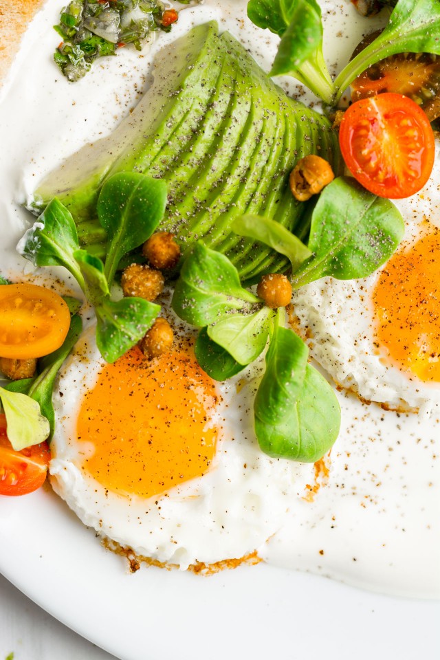 close up image of savory yogurt chimichurri salad, topped with spicy roasted chickpeas, slice avocado, tomatoes and eggs on the side
