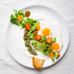 top down image of savory yogurt chimmichurri salad, topped with spicy roasted chickpeas, slice avocado, tomatoes and eggs on the side